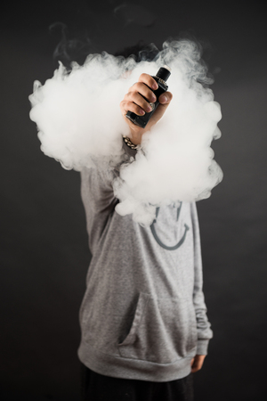 Home 54 115938859 hand of man soars on the smoke with mod in a black background vape concept